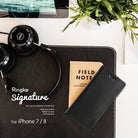 iPhone 8 / 7 Case | Signature - Black leather wallet case on a desk with headphones, a notebook, and a potted plant.