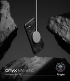 Galaxy S24 FE Case | Onyx Magnetic - Black patterned phone case suspended by a magnetic charger between dark rocks.