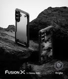 Galaxy S26 Plus Case | Fusion-X - Two Fusion-X phone cases on dark, rugged rock, one matte and one with a camo pattern.