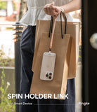 Holder Link Spin - A person holding brown shopping bags with a smartphone attached to a pink wrist strap.