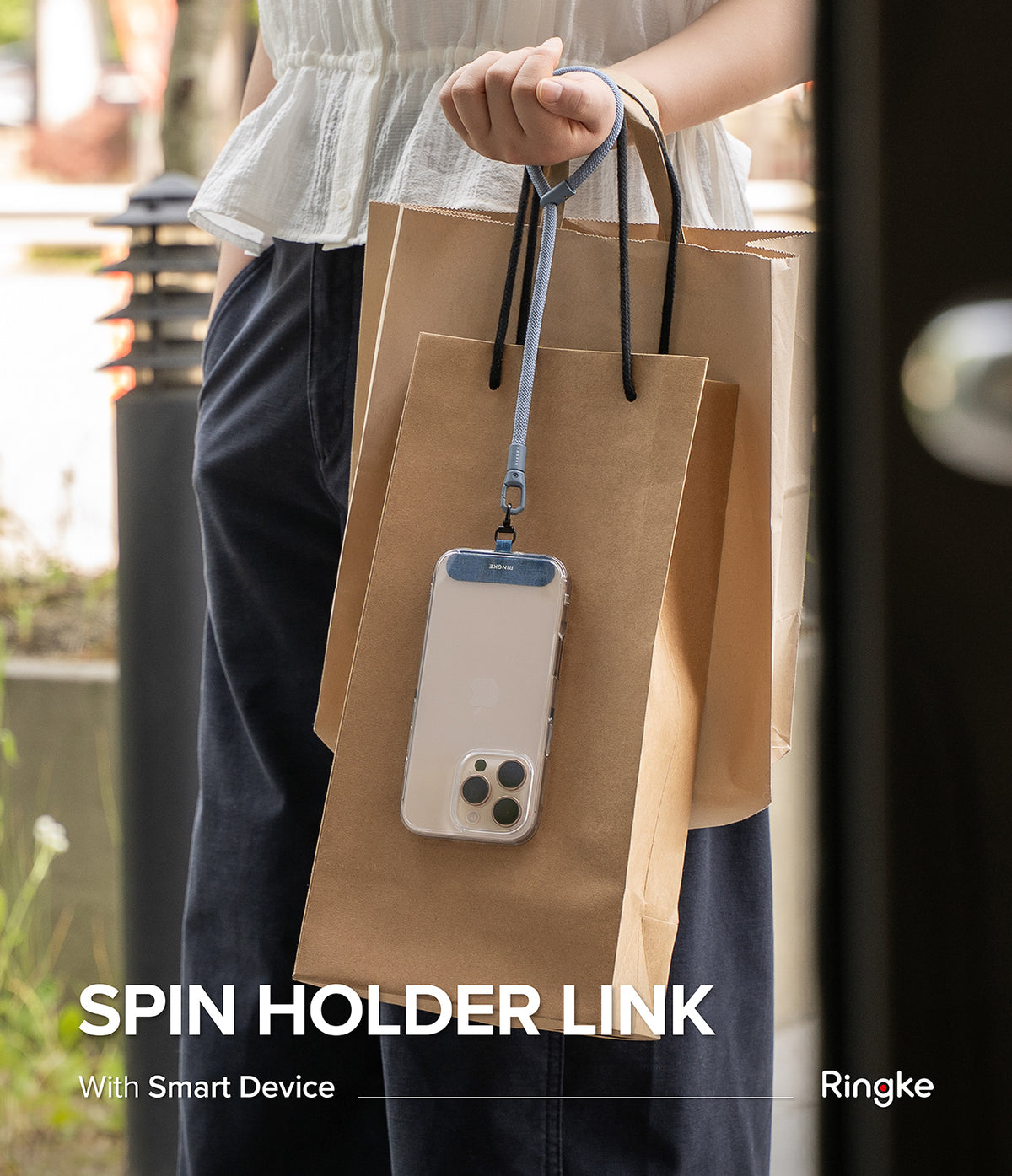 Holder Link Spin - A person holding brown paper shopping bags with a phone attached to a blue wrist strap lanyard.