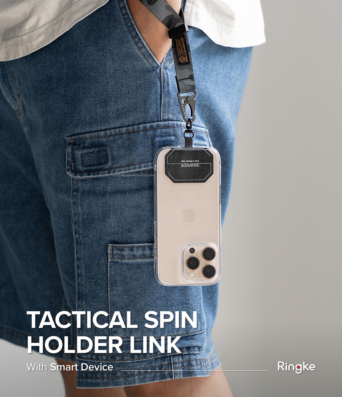 Holder Link Tactical Spin - Smartphone in a clear case attached to a tactical lanyard hanging from blue denim shorts.