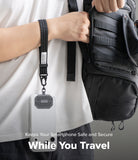 Holder Link Tactical Webbing Hand Strap - A close-up of a person wearing a white t-shirt and carrying a black backpack, demonstrating a black smartphone pouch with a detachable wrist strap hanging from their shoulder pocket. The text overlay at the bottom reads 'Keeps Your Smartphone Safe and Secure While You Travel'.