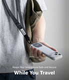 Holder Link Tactical Webbing Lanyard Strap - A person wearing a gray t-shirt and khaki jacket holds a smartphone in a clear case with a black magnetic strap attached, shown against a neutral gray background with text overlay 'Keeps Your Smartphone Safe and Secure While You Travel'.