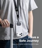 Holder Link Tactical Webbing Lanyard Strap - A person wearing a gray t-shirt and dark jeans carries a clear phone case with a black lanyard and magnetic cover, holding the handle of a silver suitcase. The image features a gray background and text overlay that reads 'Have a Safe Journey'.