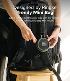 Mini Pouch | Tambourine Bag - Hands attaching a round olive green mini pouch to the strap of a black backpack.