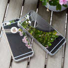 iPhone 6s / 6 Case | Mirror - Two reflective mirror-finish phone cases resting on a wooden table, reflecting nearby flowers.