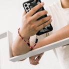 Paracord Lanyard Wrist Strap [6 Pack] - Person holding a smartphone with a red and black paracord wrist strap attached.