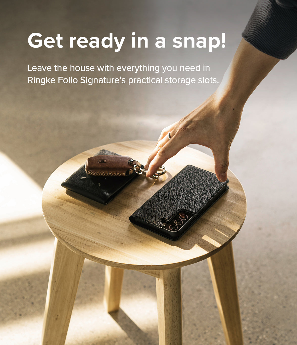 Galaxy S22 Case | Folio Signature Standard - Hand reaching for a black leather phone case and wallet on a wooden stool.